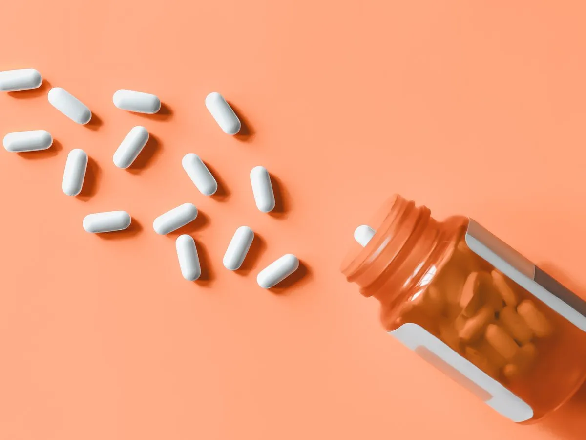 Gélules blanches s'échappant d'un flacon de médicaments orange